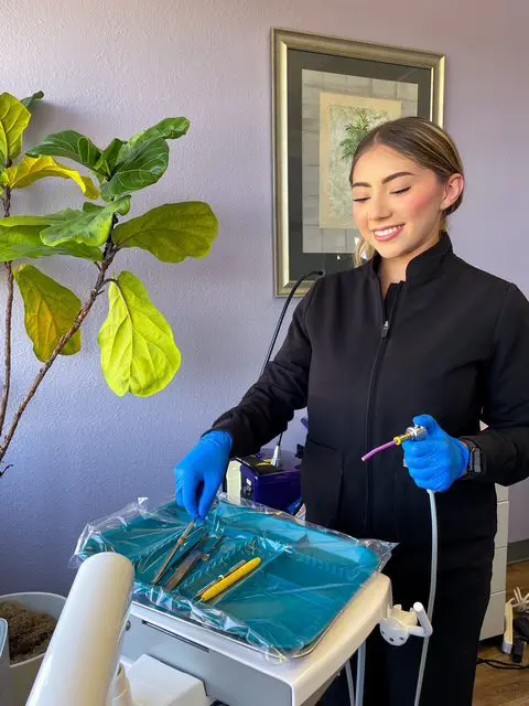 A woman in blue gloves preparing dental tools on a tray.