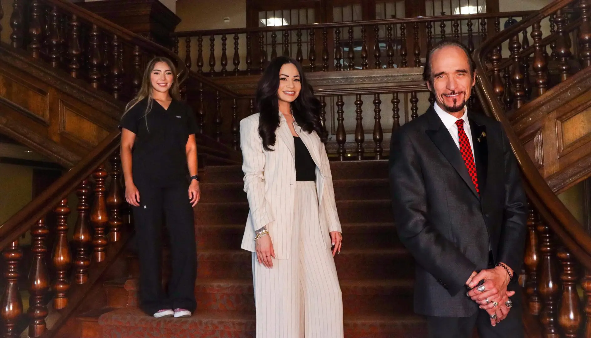 Three professionals posing confidently on a staircase indoors.