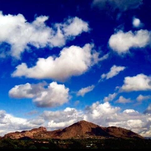 Blue sky with white clouds over a mountainous landscape.